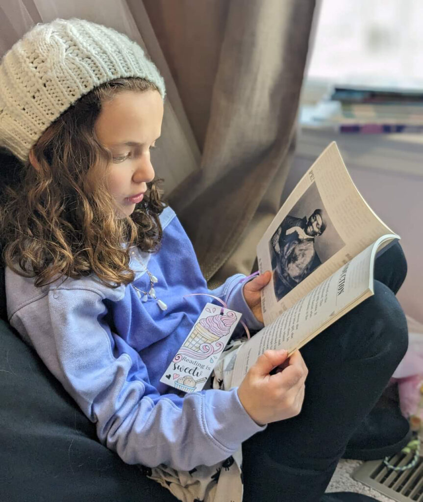An elementary-aged girl reading a kid's book from Anna's Books
