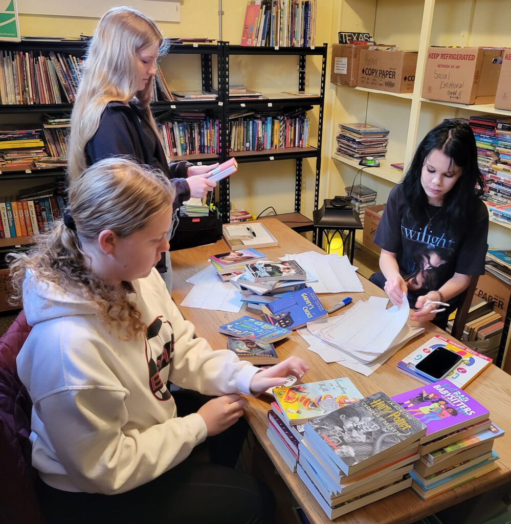 three teenage members of a girl scout troop volunteer at anna's books by labeling book donations